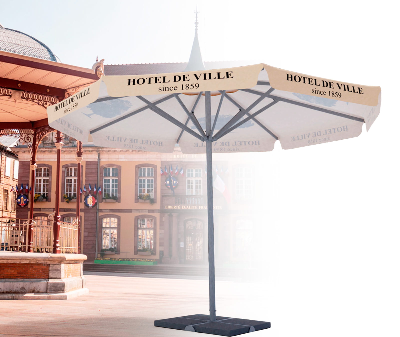 Sonnenschirm mit dem Aufdruck 'HOTEL DE VILLE since 1859', auf einem Platz vor einem historischen Gebäude.