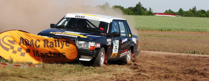 Ein Rallye-Auto fährt durch einen Feldweg und kollidiert mit einer Werbebande des ADAC Rallye Masters.