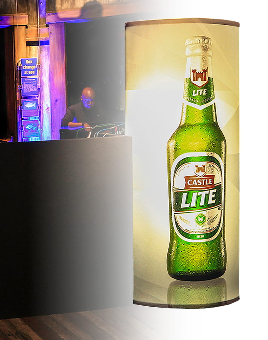 Säule mit Werbung für Castle Lite Bier, im Hintergrund ein DJ an einem Mischpult.
