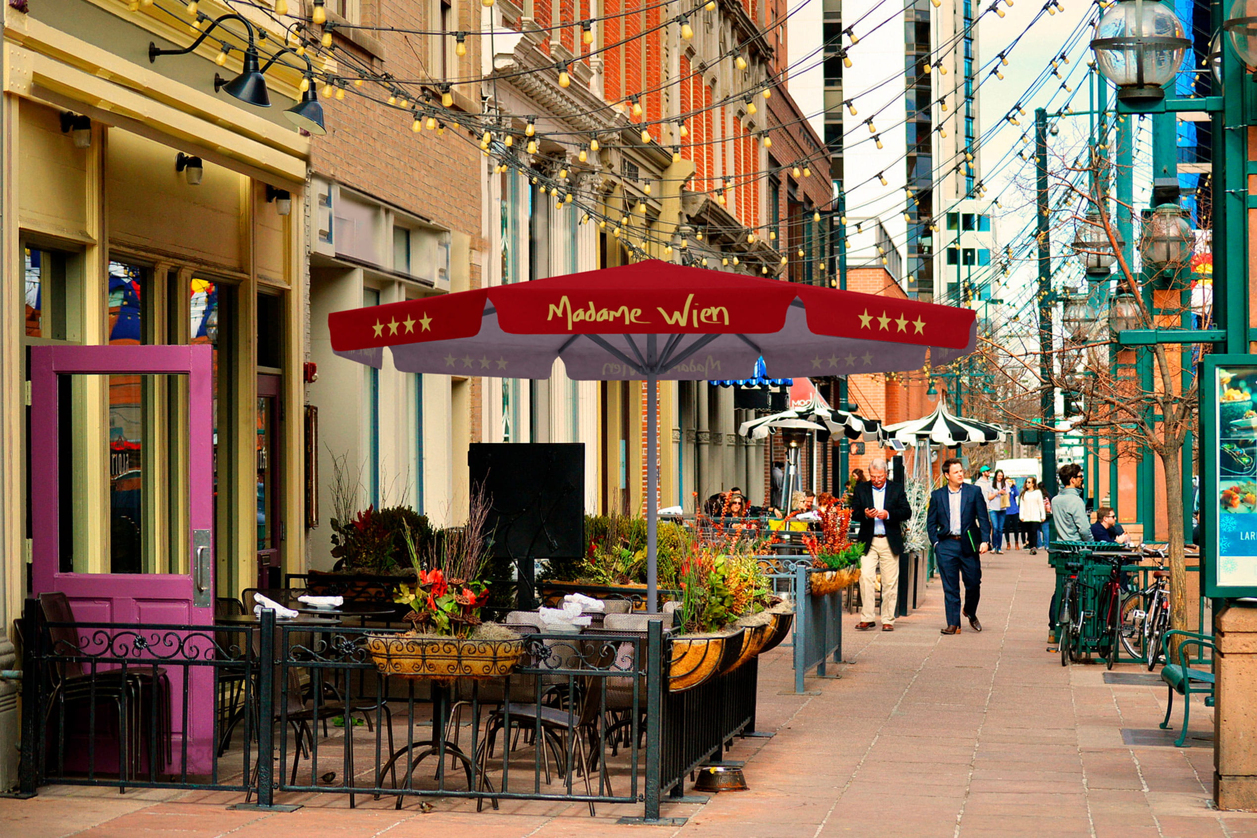 Sonnenschirm 'Expert Madame Wien' über einem Restaurant im Freien, umgeben von Pflanzen und beleuchteten Straßen.