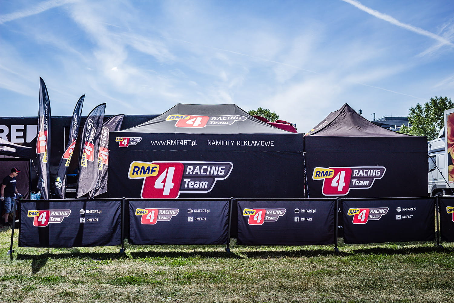 Zelt und Banner des RMF 4 Racing Teams bei einer Rennsportveranstaltung, mit schwarzem Design und rotem Logo.