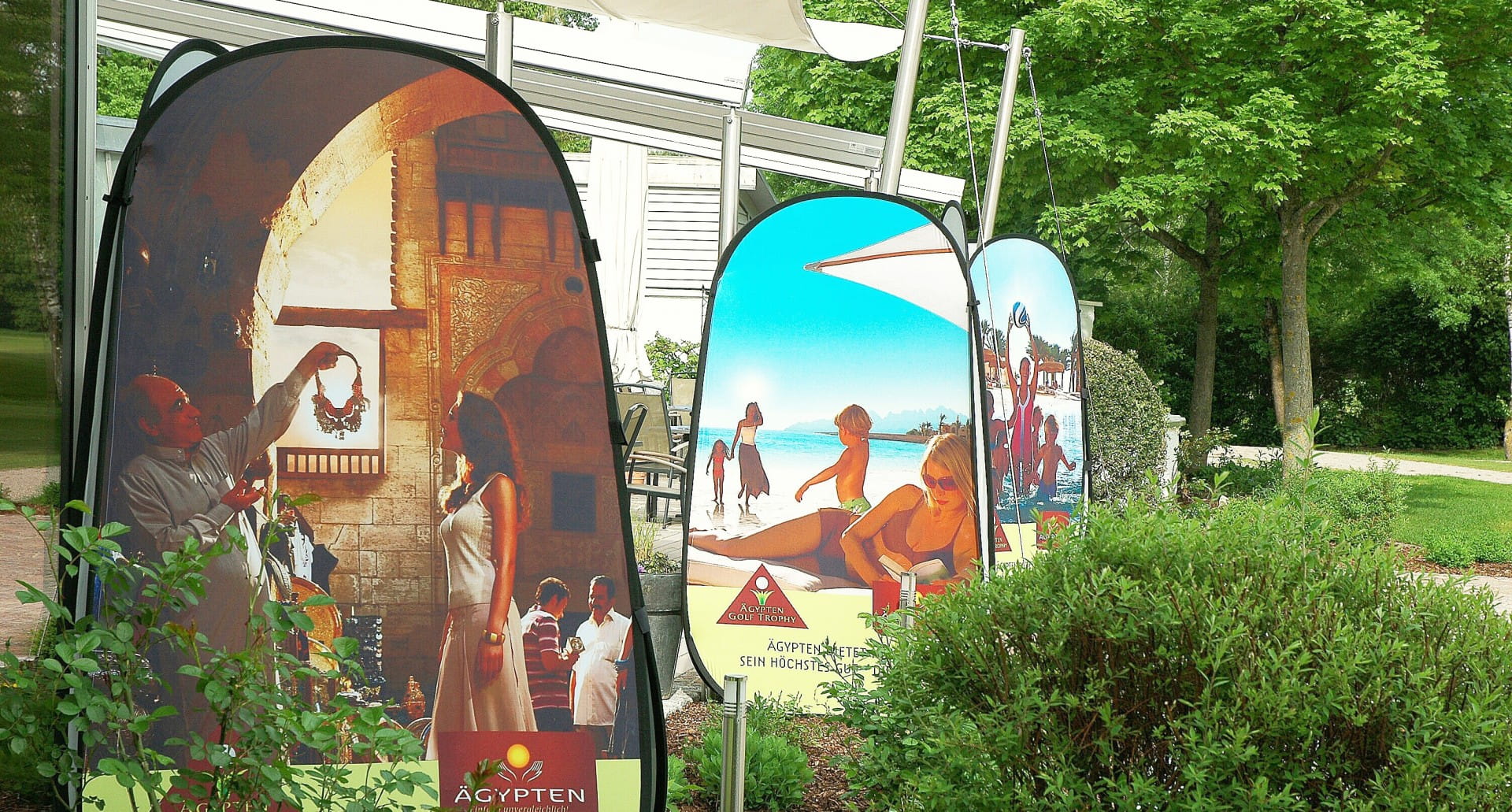 Werbesäule Quicktower mit ägyptischen Motiven, darunter eine Marktszene und Strandansicht.