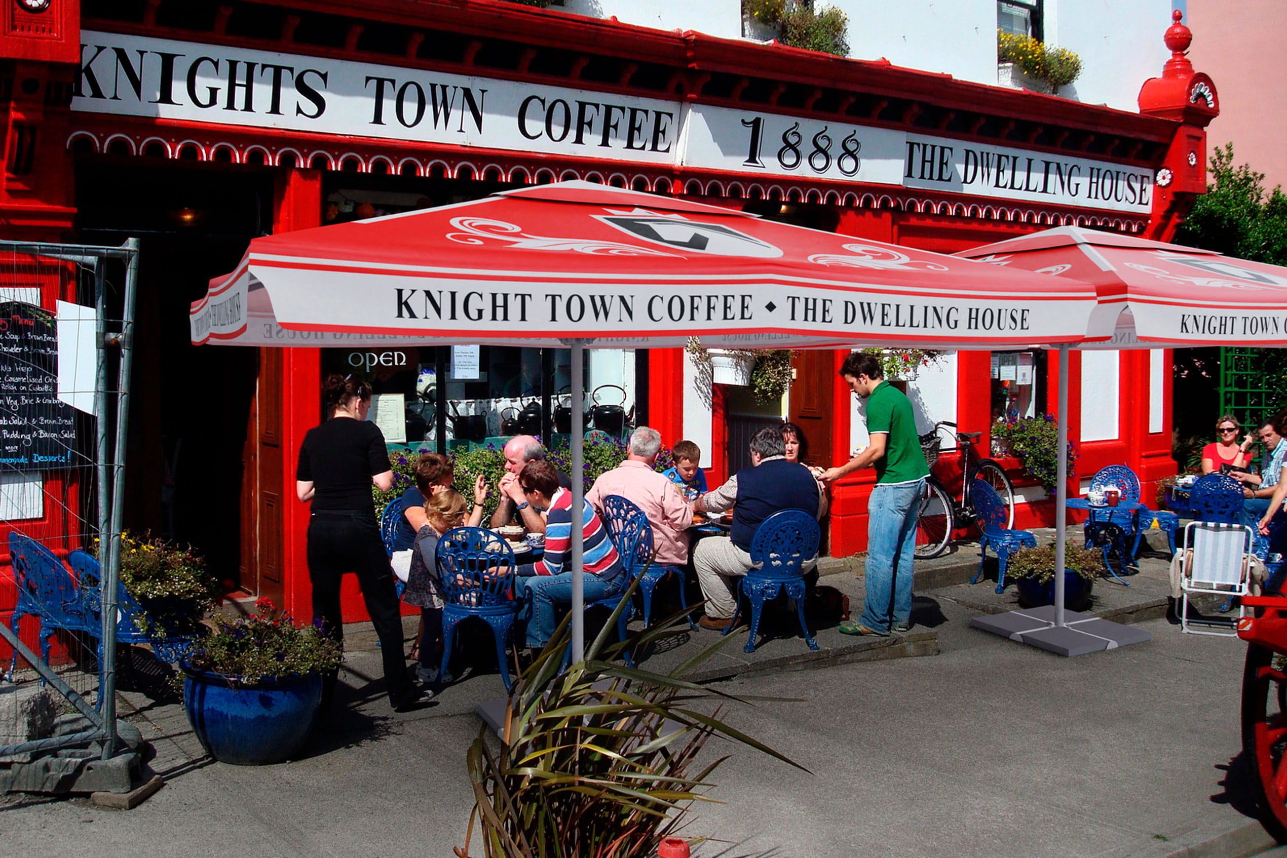 Sonnenschirm Expert Knights vor dem Knights Town Coffee, Gäste sitzen an Tischen im Freien.