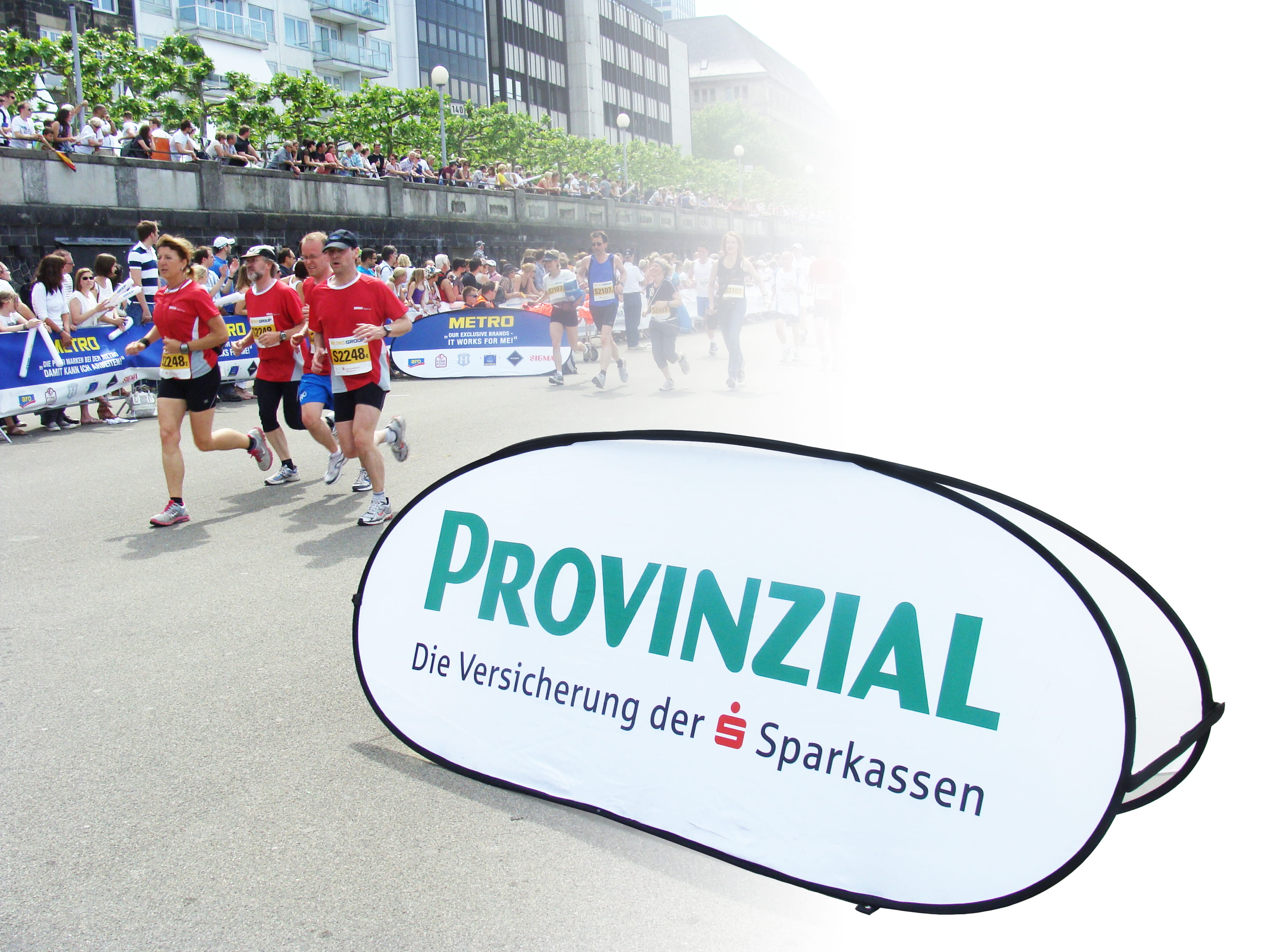 Werbebande mit dem Schriftzug 'PROVINZIAL Die Versicherung der Sparkassen' bei einem Lauf-Event, im Hintergrund Läufer und Zuschauer.
