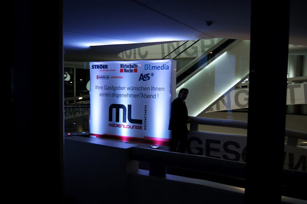 Beleuchtete Messewand mit dem Text 'Ihre Gastgeber wünschen Ihnen einen angenehmen Abend!' und dem Logo 'ML Medienlounge München'.