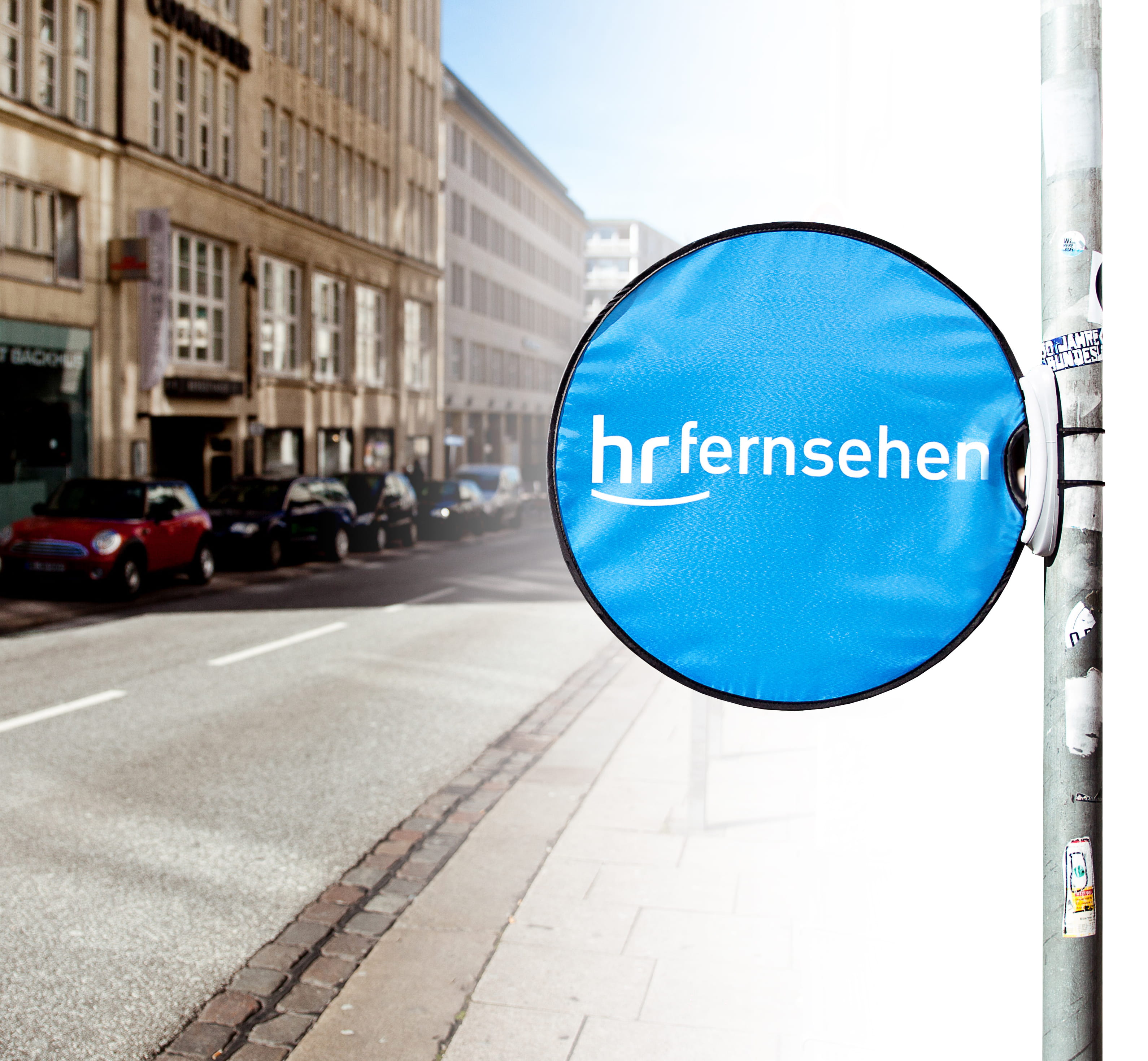 Werbedisplay Easydisc Flex von ENTDECKER in blauer Farbe mit dem Logo 'hr fernsehen', montiert an einem Straßenpoller.
