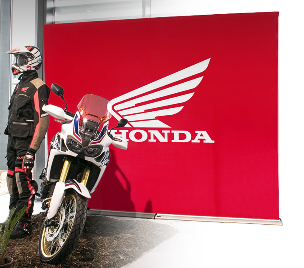 Einsatzbeispiel des Produkts 'Easywall Flex' mit einem roten Hintergrund und dem Honda-Logo, daneben ein Motorrad und ein Fahrer in Schutzkleidung.