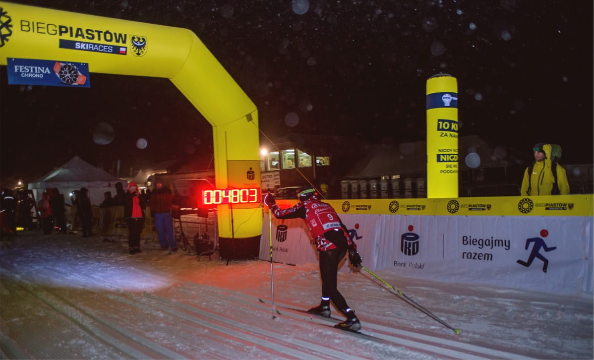 Ein Skifahrer überquert die Ziellinie bei einem Nachtrennen, mit einem beleuchteten Zielbogen und einer Zeitmessung von 7:40:03.